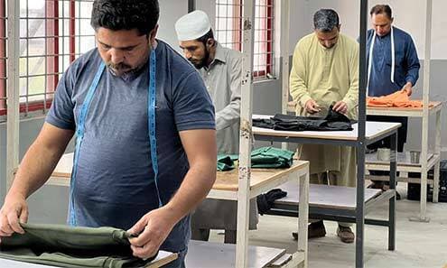 A worker checks fabric and garment measurements at a worktable.