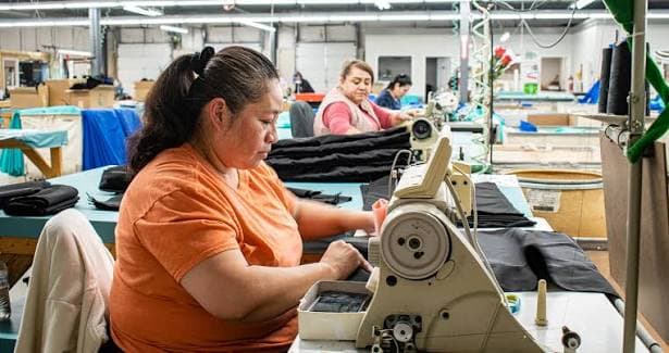 A garment worker guides dark fabric through an industrial sewing machine.