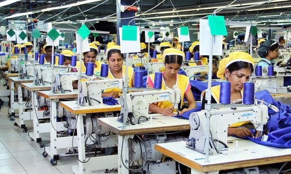 Garment workers operating industrial sewing machines in a production room.
